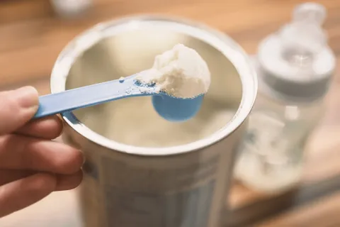 A spoonful of instant formula being taken out of a larger container