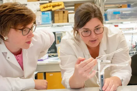 Katharina Maisel and Jenna Mueller in white lab coats looking at an applicator in the lab