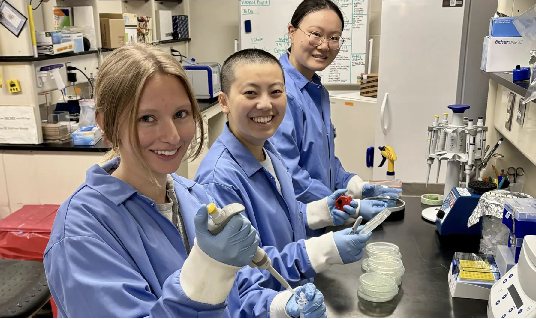 Three Student researchers in a lab, wearing lab coats posing for a photo