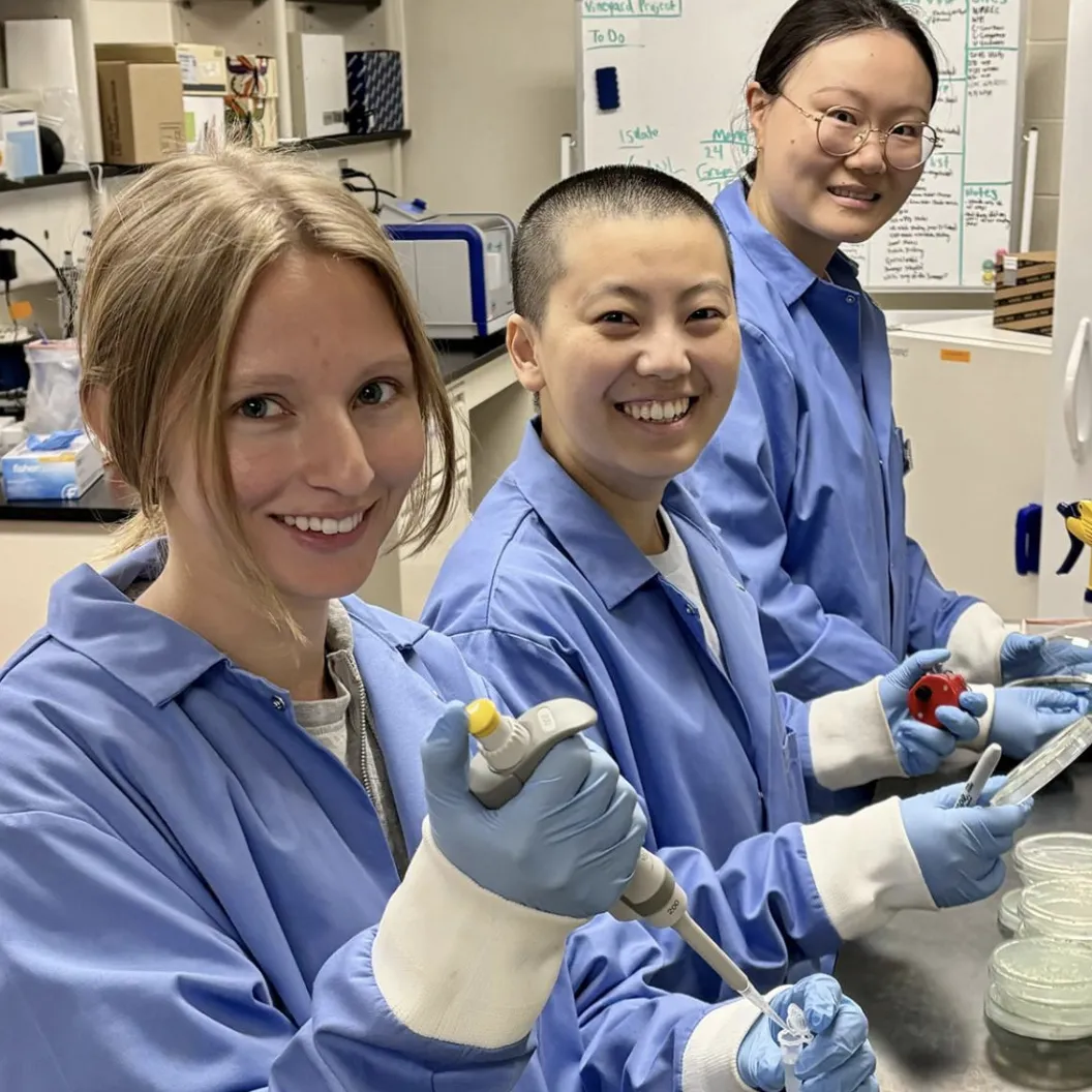 ThreeStudent researchers in a lab, wearing lab coats posing for a photo